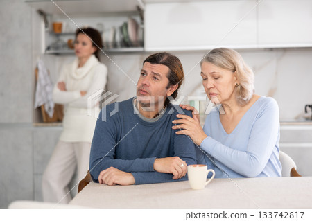 Senior woman sits near adult son and comforts him during quarrel with wife. Senior woman sits near adult son and comforts him during quarrel with wife. 133742817