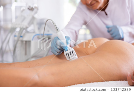 Cosmetologist using cold hammer for hardware procedure on buttocks of woman Cosmetologist using cold hammer for hardware procedure on buttocks of woman 133742889