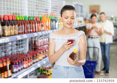 Young Asian woman using smartphone for mobile payment for sauce in store Young Asian woman using smartphone for mobile payment for sauce in store 133742959
