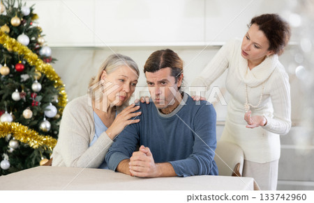 Senior woman sits near adult son and comforts him in quarrel with wife during winter holiday Senior woman sits near adult son and comforts him in quarrel with wife during winter holiday 133742960