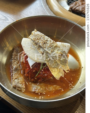 Chilled, chewy naengmyeon noodles in tangy broth paired with juicy, savory mandu dumplings, offering a perfect balance of refreshing coolness and hearty comfort in every delicious Korean bite. 133743826
