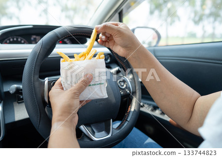 Asian lady holding French fries potato chips to eat in car, dangerous and risk an accident. Asian lady holding French fries potato chips to eat in car, dangerous and risk an accident. 133744823