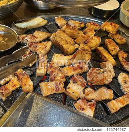 Grilled samgyeopsal, showcasing thick slices of pork belly sizzling on the grill. A popular Korean barbecue dish, capturing the essence of a delicious dining experience. Grilled samgyeopsal, showcasing thick slices of pork belly sizzling on the grill. A popular Korean barbecue dish, capturing the essence of a delicious dining experience. 133744987