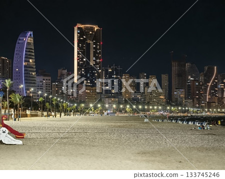 empty playground slide on sandy promenade with illuminated towers palm trees empty playground slide on sandy promenade with illuminated towers palm trees 133745246