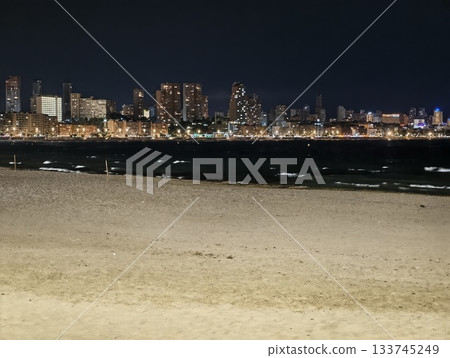 gentle tide lapping dark shoreline with city lights small breakers textured sand gentle tide lapping dark shoreline with city lights small breakers textured sand 133745249