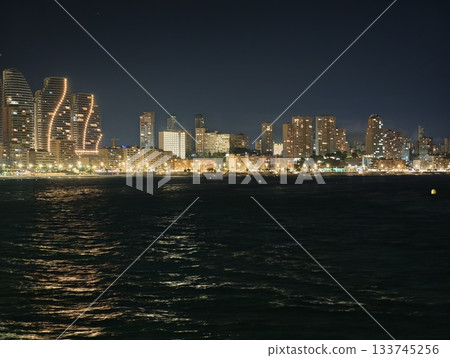 calm bay under city lights, quiet night scene featuring skyline reflections and gentle waves 133745256