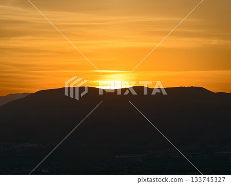 golden sunset behind mountain silhouettes, twilight bathes city and mountain outlines in gold 133745327