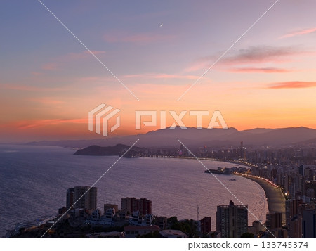 beach sunset serenity, warm sunset over gentle waves, golden hour on sandy shores and city skyline 133745374