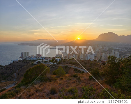 hiking at sunset overlooking coast, coastal city sunset viewed from hillside with rugged paths 133745401