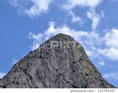 rugged peak with clouds and shadows, towering rocky summit piercing clouds with raw texture 133745507