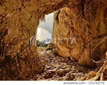 sunlit cave opening with harbor and boats, goldenlit cave entrance revealing busy harbor and masts 133745578