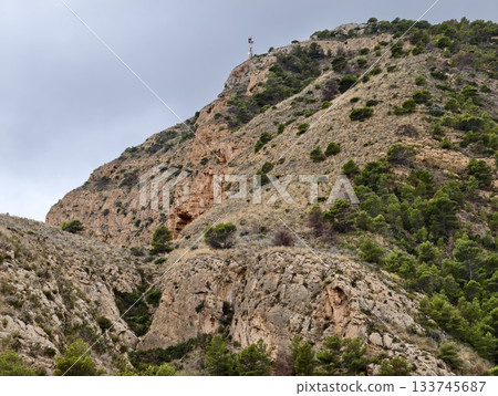 steep cliff featuring summit marker and cave, sharp cliffside with summit marker and hidden cave 133745687