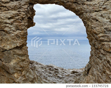 windblown waves crash against rocky shoreline beneath brooding overcast sky and distant horizon windblown waves crash against rocky shoreline beneath brooding overcast sky and distant horizon 133745728