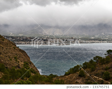 town across bay under low clouds waterfront buildings faintly visible beyond choppy sea town across bay under low clouds waterfront buildings faintly visible beyond choppy sea 133745731