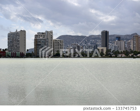 dense highrise cityscape beside peaceful green lake with mountain view and subtle reflections 133745753