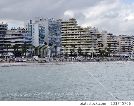 crowded shoreline with tourism activity, bustling sandy beach promenade featuring sunbathers crowded shoreline with tourism activity, bustling sandy beach promenade featuring sunbathers 133745766