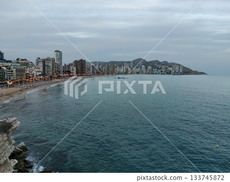 cityscape by rocky coast, dramatic rocky shoreline juxtaposed with city buildings and distant hills 133745872