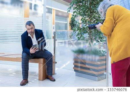 Female photographer shooting a businessman reading an ebook in a bright modern office. High quality photo Female photographer shooting a businessman reading an ebook in a bright modern office. High quality photo 133746076