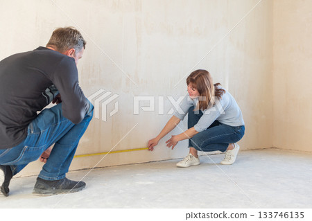 Young couple moving in new apartmen. People measure size of wall with tape measure. Concept new homes, new beginning. High quality photo Young couple moving in new apartmen. People measure size of wall with tape measure. Concept new homes, new beginning. High quality photo 133746135