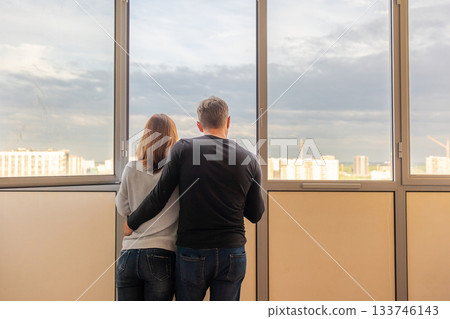 Man hugging his wife. Young couple moving in new apartmen. People looks out window at new houses. Concept new homes, new beginning. High quality photo 133746143