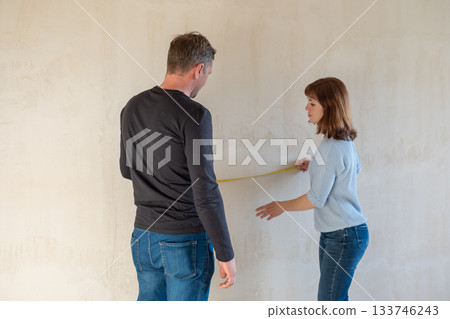 Young couple moving in new apartmen. People measure size of wall with tape measure. Concept new homes, new beginning. High quality photo 133746243
