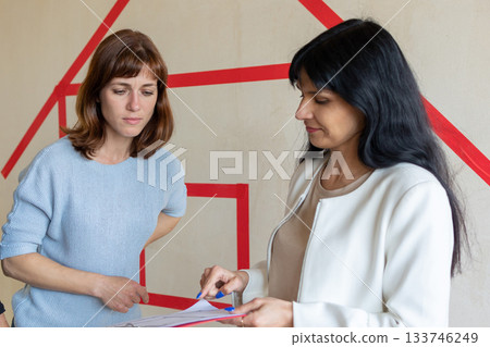 Realtor signs contract, shows plan of apartment in new building to young couple. Concept new homes, new beginning. High quality photo 133746249