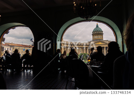 View of Kazan Cathedral from Singer Cafe through window. Silhouettes of people sitting at tables in old Singer House in Saint-Petersburg, Russia. High quality photo 133746334