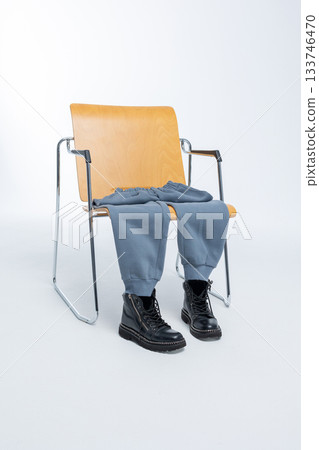 Gray sweatpants with black boots lying on wooden chair on light background. Vertical photo. High quality photo Gray sweatpants with black boots lying on wooden chair on light background. Vertical photo. High quality photo 133746470