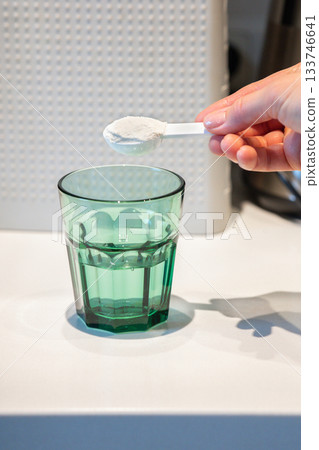Woman's hand pours white powder with medicine into transparent glass of water with spoon. High quality photo Woman's hand pours white powder with medicine into transparent glass of water with spoon. High quality photo 133746641