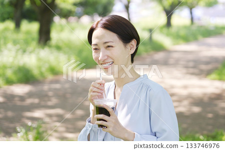 A woman in her 40s drinking iced coffee outdoors A woman in her 40s drinking iced coffee outdoors 133746976