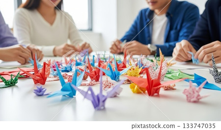 Asian people folding colorful origami paper cranes together in bright workshop classroom during creative art therapy session 133747035