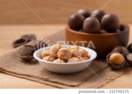 Peeled and unpelled macadamia nuts in a bowl on brown background Peeled and unpelled macadamia nuts in a bowl on brown background 133748175