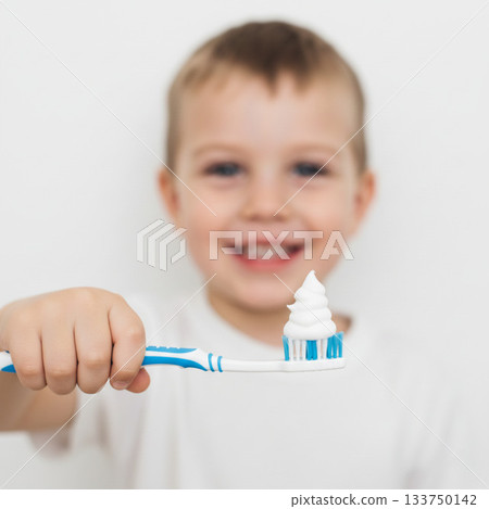 A smiling young boy holds a toothbrush with a swirl of white toothpaste in shape of a Christmas tree. The toothbrush features blue and white colors 133750142