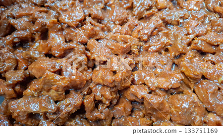 Macro Shot of Beef Chunks Coated in Thick, Red Rendang Sauce during Cooking 133751169