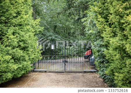 A black iron gate stands between dense green walls, silent under the weight of summer air. A black iron gate stands between dense green walls, silent under the weight of summer air. 133752616