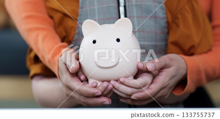 Financial Literacy. Parent teaching child about saving money with piggy bank. 133755737