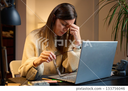 Tired woman with headache working on laptop at home office Tired woman with headache working on laptop at home office 133756046