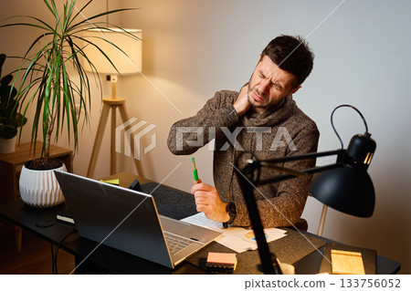 Man with neck pain working at desk in home office 133756052