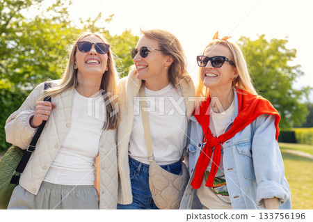 Happy friends enjoy sunny outdoor moment with bright smile and relaxed vibe. Warm sunlight creates cheerful atmosphere, highlighting friendship, joy and carefree mood during weekend walk 133756196