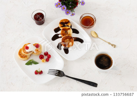 Cup of coffee and curd fritters with sour cream, berries and chocolate on the porcelain plates. 133756687