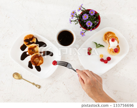 Cup of coffee and curd fritters with sour cream, berries and chocolate on the porcelain plates. Cup of coffee and curd fritters with sour cream, berries and chocolate on the porcelain plates. 133756696