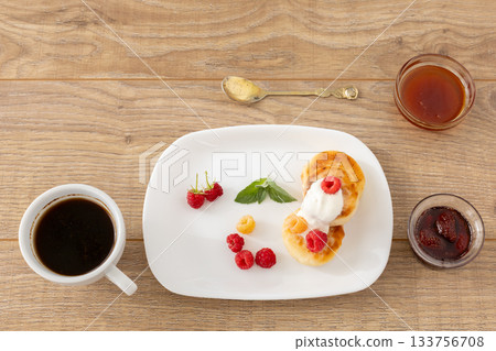 Cup of coffee and curd fritters with sour cream and berries on the porcelain plates. 133756708