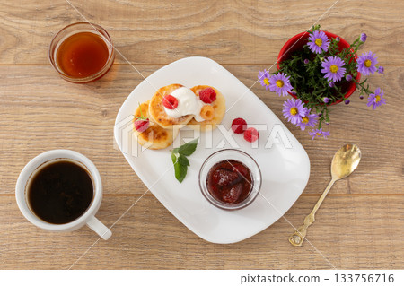 Cup of coffee and curd fritters with sour cream and berries on the porcelain plates. Cup of coffee and curd fritters with sour cream and berries on the porcelain plates. 133756716