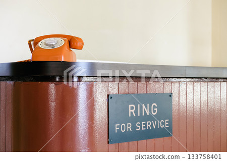 Retro orange telephone in public service station waiting for customers to call 133758401