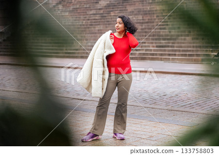 indian woman in red sweater holding winter coat on city street in helsinki indian woman in red sweater holding winter coat on city street in helsinki 133758803