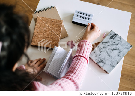 Person sits at white table touching FRESH START light box next to small open notebook and planner covers. Creative journaling, New Year goals, visual goal setting, productivity planning. 133758916