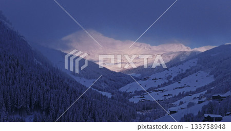 Aerial photo of snowy alpine peaks in Austria with a glacier rising through morning mist. Blue sky, sunlight, and conifer forests in the foreground create a peaceful winter atmosphere. Aerial photo of snowy alpine peaks in Austria with a glacier rising through morning mist. Blue sky, sunlight, and conifer forests in the foreground create a peaceful winter atmosphere. 133758948