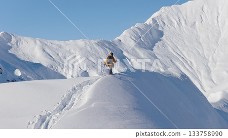 Aerial photo of a ski mountaineer ascending a snowy alpine ridge in Austria. Winter landscape, backcountry adventure, and solitude in breathtaking mountain scenery. 133758990