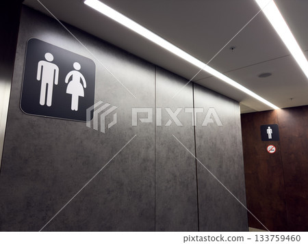 Modern hallway interior with gentleman and lady sign. Gender separated restroom symbol on wall in front of restroom entrance. Public restroom hygiene concept Modern hallway interior with gentleman and lady sign. Gender separated restroom symbol on wall in front of restroom entrance. Public restroom hygiene concept 133759460