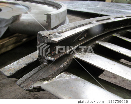 Close-up view of damaged metal component, possibly from turbine or industrial machinery. Jagged edges, evidence of repair work, like welding, are visible on the worn surface. Restoration of diaphragms 133759626